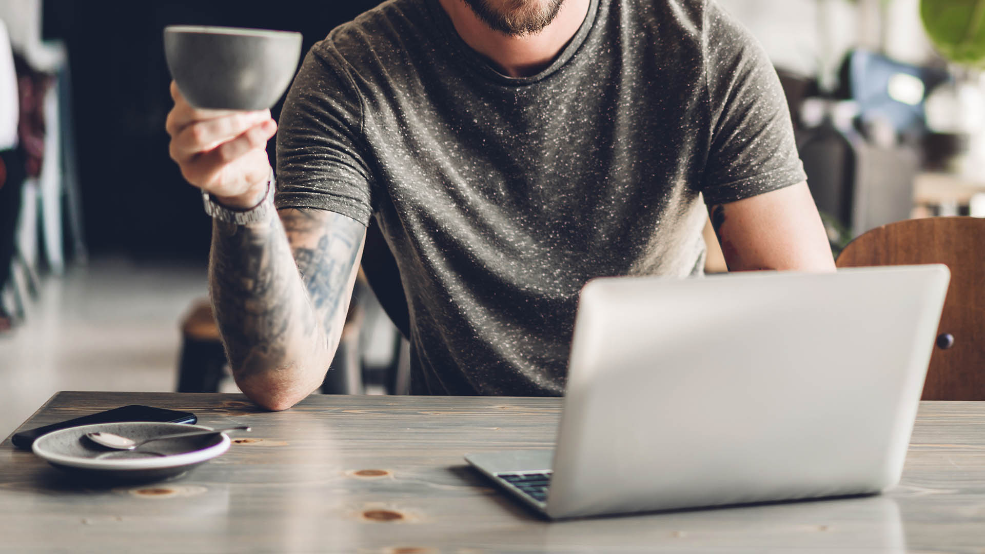 Person drinking coffee and working on laptop at table.