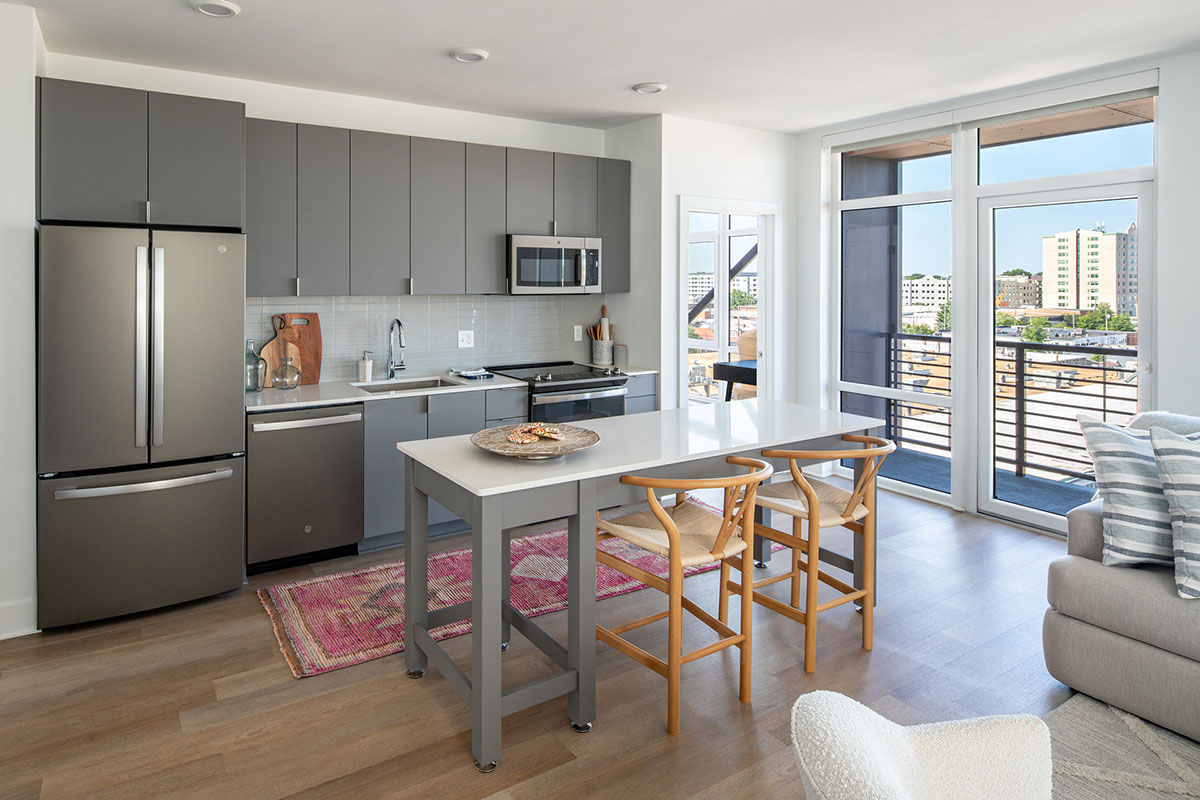 Kitchen with wood floor, grey cabinets, white counters, and stainless steel appliances.
