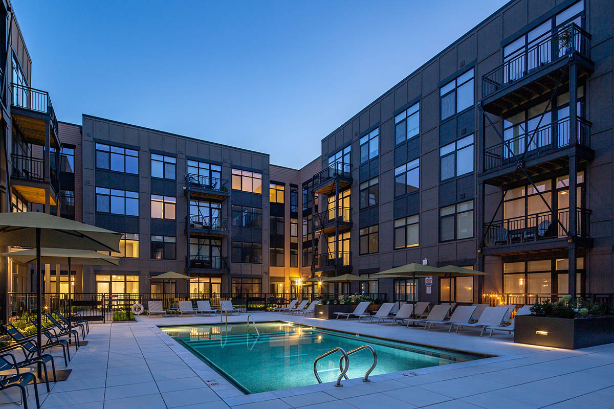 Pool area at night with glowing pool, lounge chairs, and umbrellas.